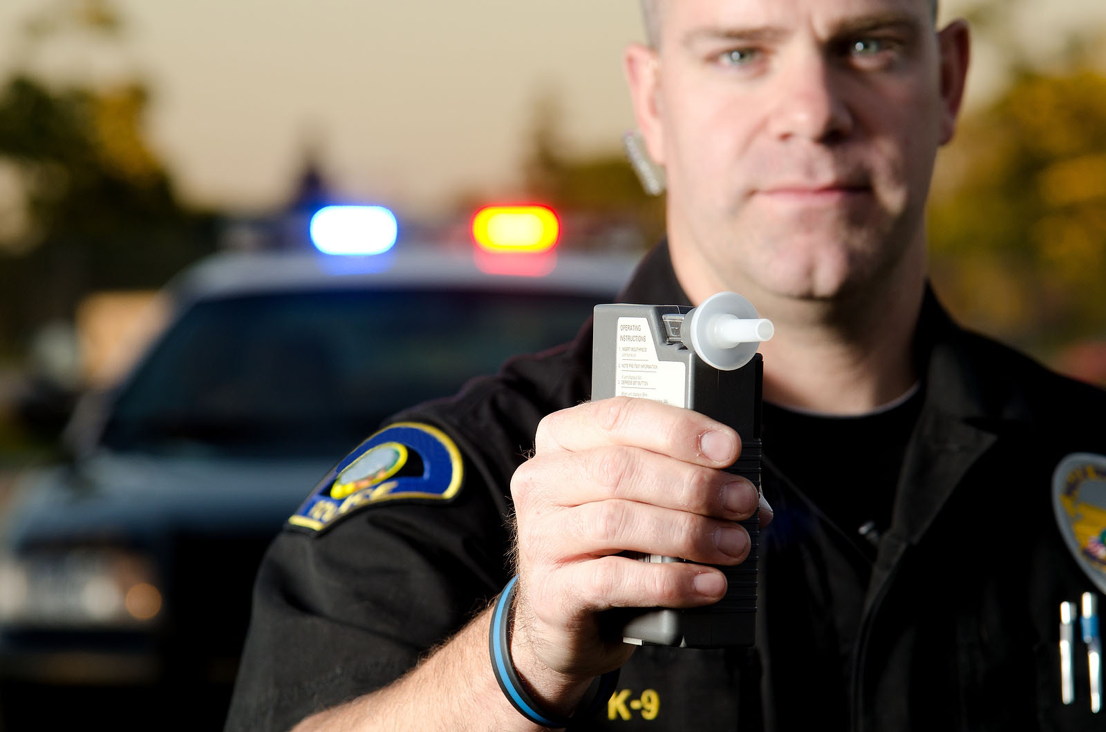 A police officer holding a breath test machine with his police car in the background for a DUI Charge concept